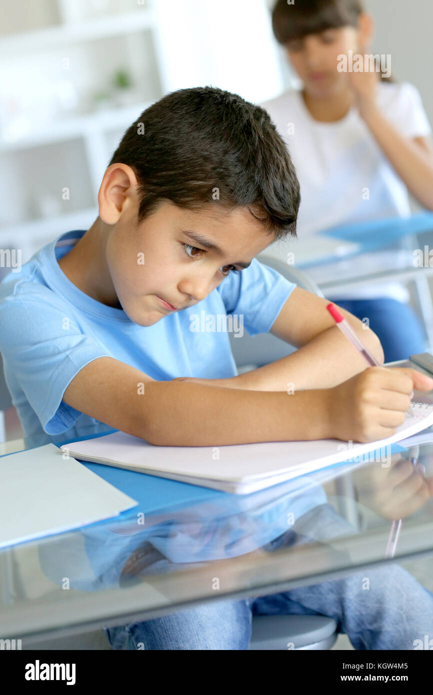 Primo piano del giovane ragazzo iscritto su notebook a scuola Foto Stock