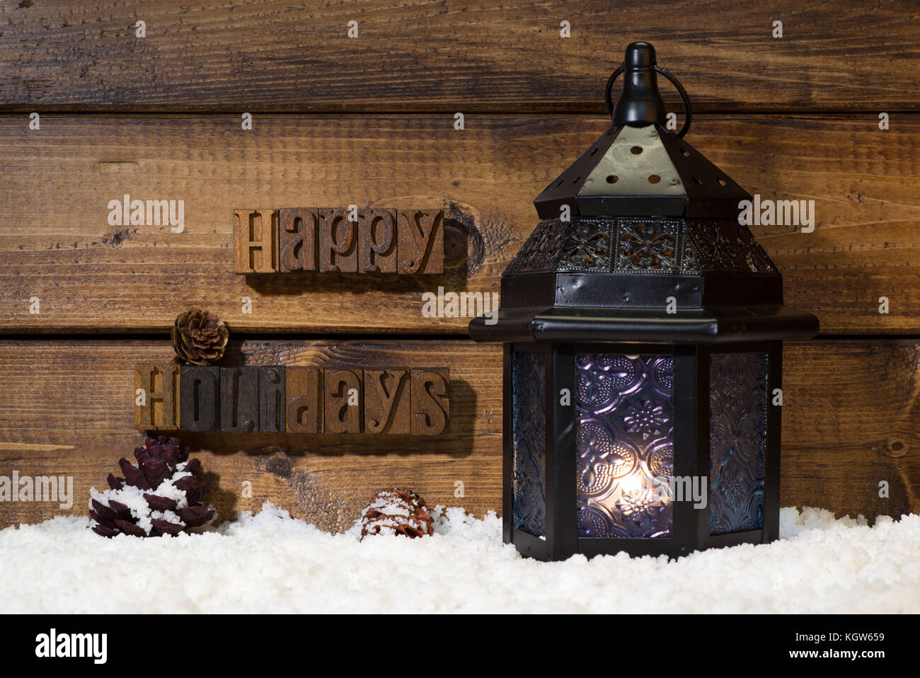 Vacanze felici di testo su un sfondo di legno con la lanterna di masterizzazione sulla neve Foto Stock