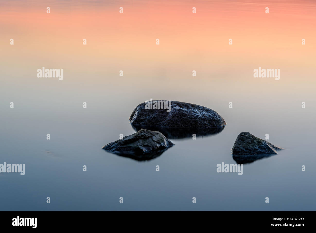 Bella abstract rosa e azzurro sfondo decorativo con una superficie liscia dell'acqua e pietre al tramonto, presa su una lunga esposizione Foto Stock