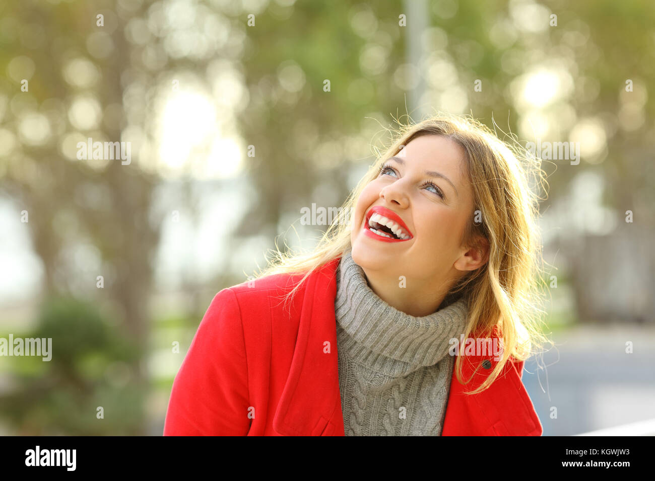 Ritratto di una ragazza felice che indossa una giacca rossa e jersey ridendo e guardando al di sopra all'aperto in un parco con spazio di copia Foto Stock