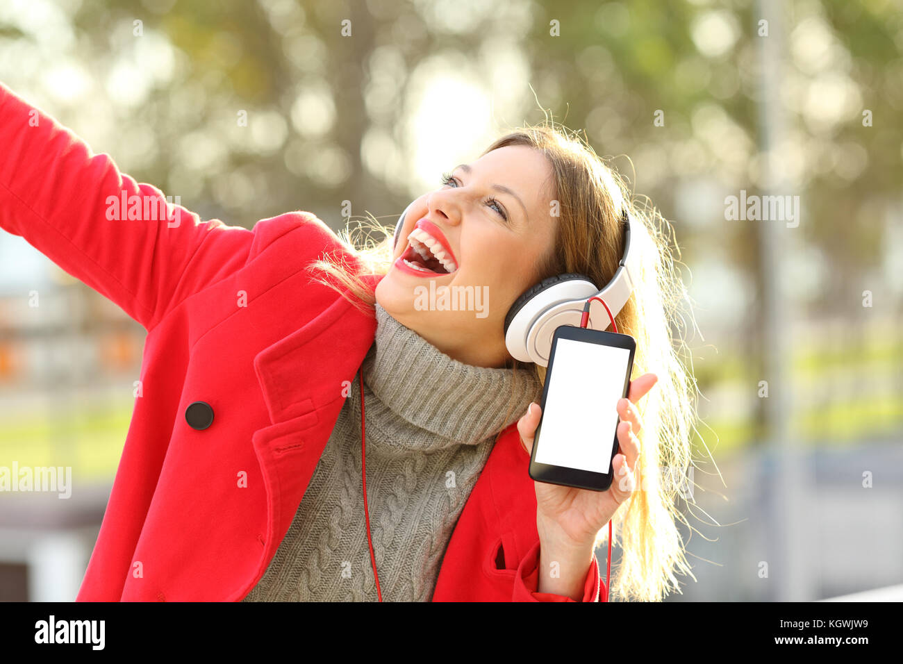 Donna felice ascoltando musica e ballando mostra smart phone al di fuori dello schermo in un parco in inverno Foto Stock