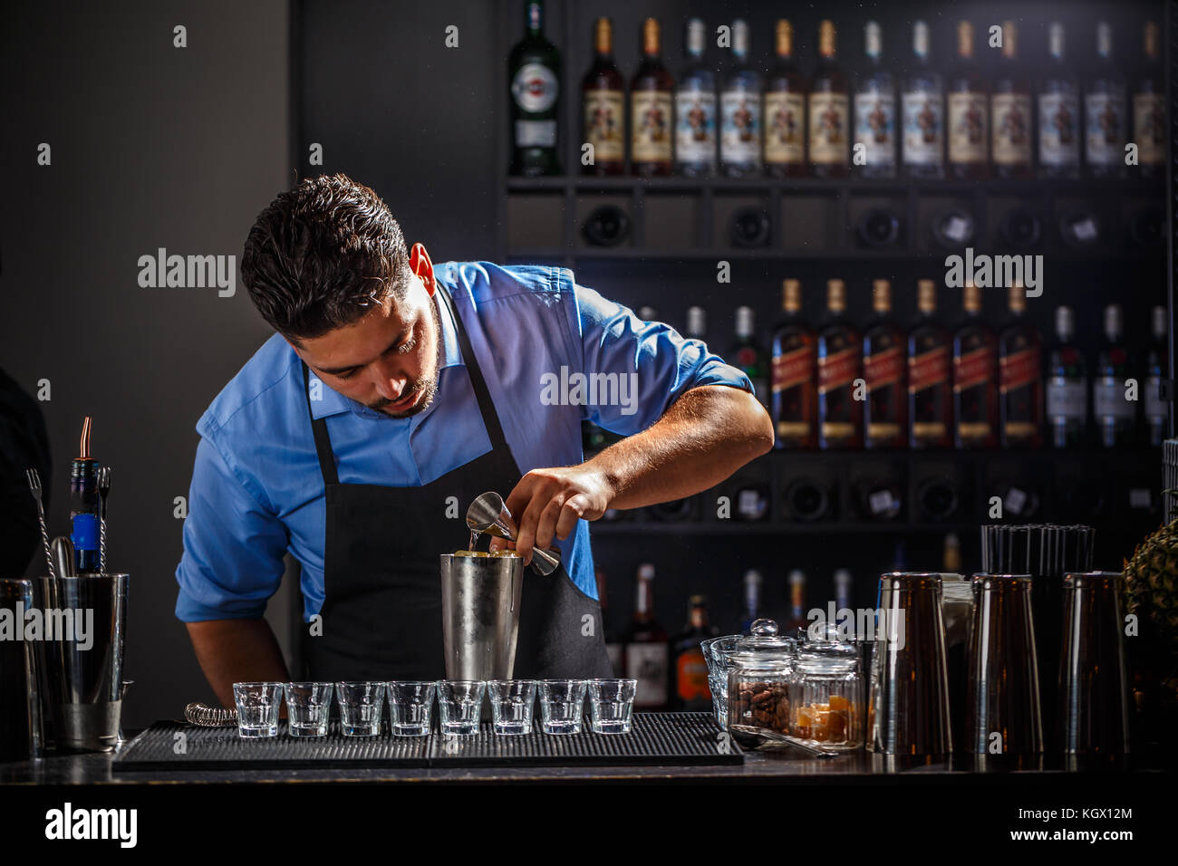 Barista con jigger di colata di alcol in shaker e la preparazione di cocktail al bancone bar Foto Stock