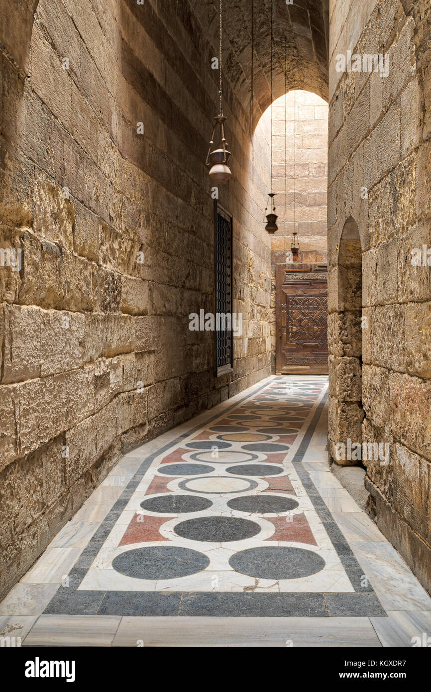 Corridoio ad arco che conduce al cortile del sultano barquq moschea con  mattoni di pietra a parete, ornata di marmi colorati pavimenti e porte in  legno, vecchio cairo, Egitto Foto stock -