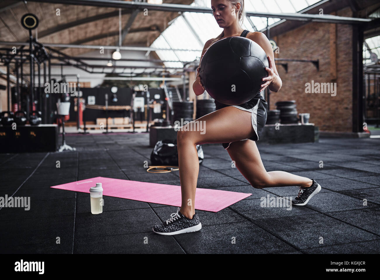 Montare la giovane donna bionda in sportswear lavorando fuori da solo in una palestra facendo esercizi di nucleo con una sfera svizzero Foto Stock