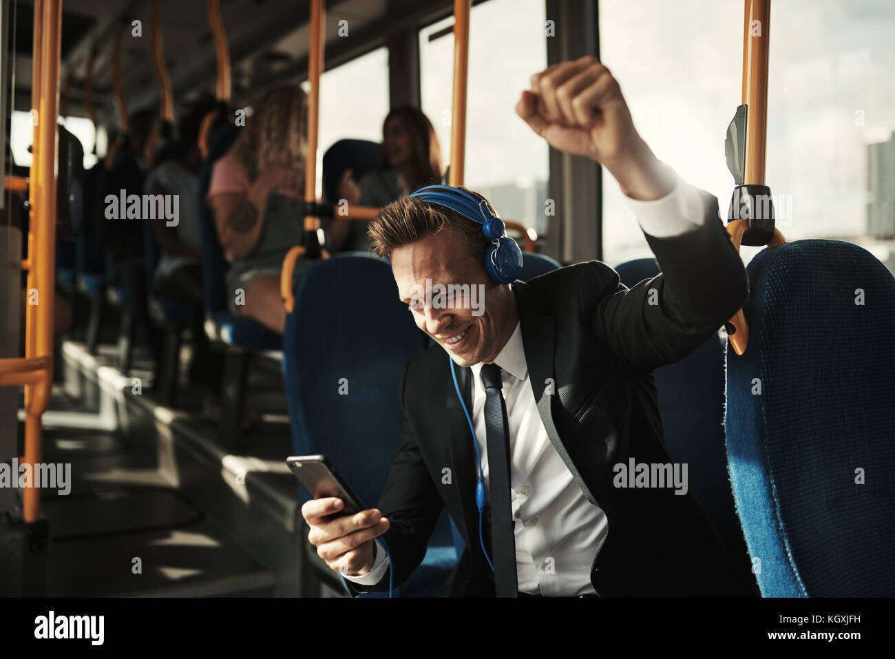Sorridente giovane impreditore pugno il pompaggio di aria mentre seduti su un autobus durante i suoi spostamenti di mattina per ascoltare musica sullo smartphone e le cuffie Foto Stock