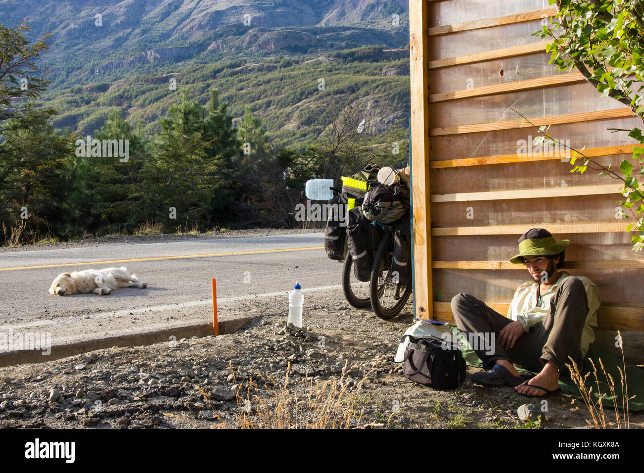 Povero viaggiatore uomo in attesa per un giro in prossimità di una strada dove nessuno passa con un cane dorme sulla strada Foto Stock