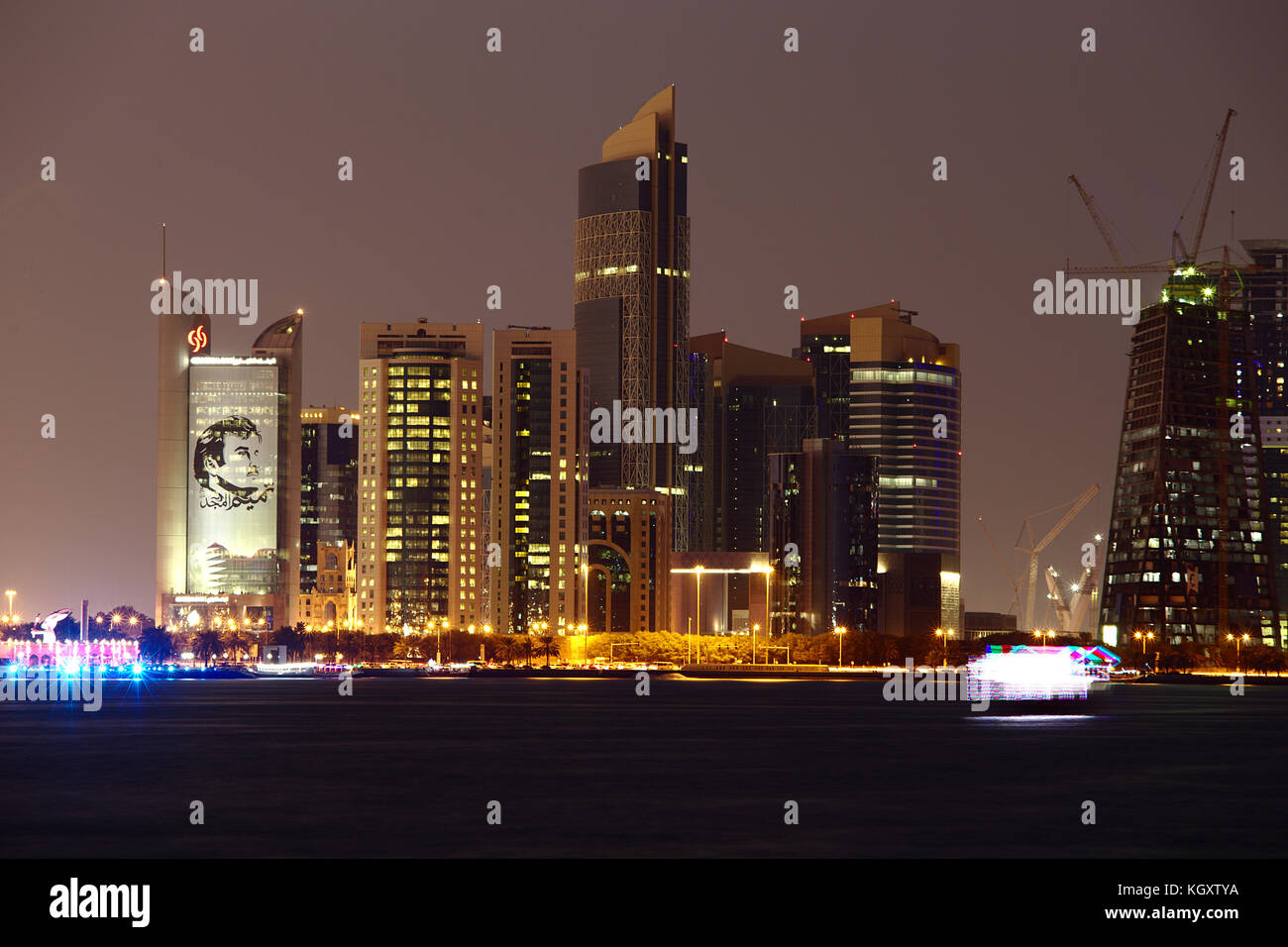 Doha, Qatar - 11 novembre 2017: skyline della città di notte con la banca commerciale dalla torre e poster di Emir Tamim Bin Hamad sulla sinistra. una luminosa Foto Stock