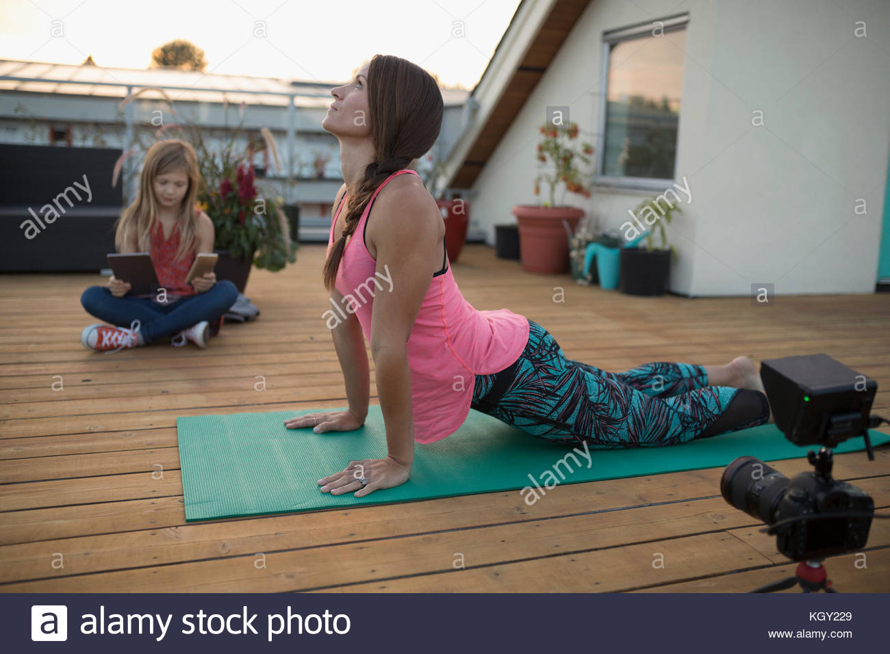 Istruttore di yoga femminile con video macchina fotografica filma, vlogging verso l'alto cane yoga posa sul patio ponte Foto Stock