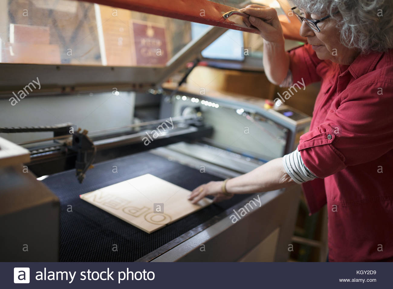 Machinista donna anziana che mette Open sign in taglierina laser in officina Foto Stock