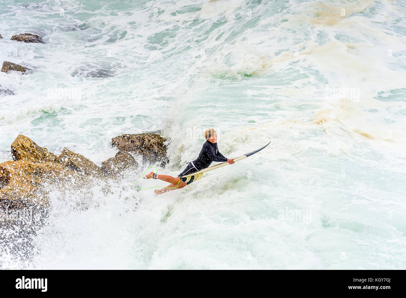 Un surfista si tuffa nell'acqua di zangolatura di una massiccia giornata di surf da rocce vicino alla spiaggia di Bronte rock pool di Sydney, NSW, Australia Foto Stock