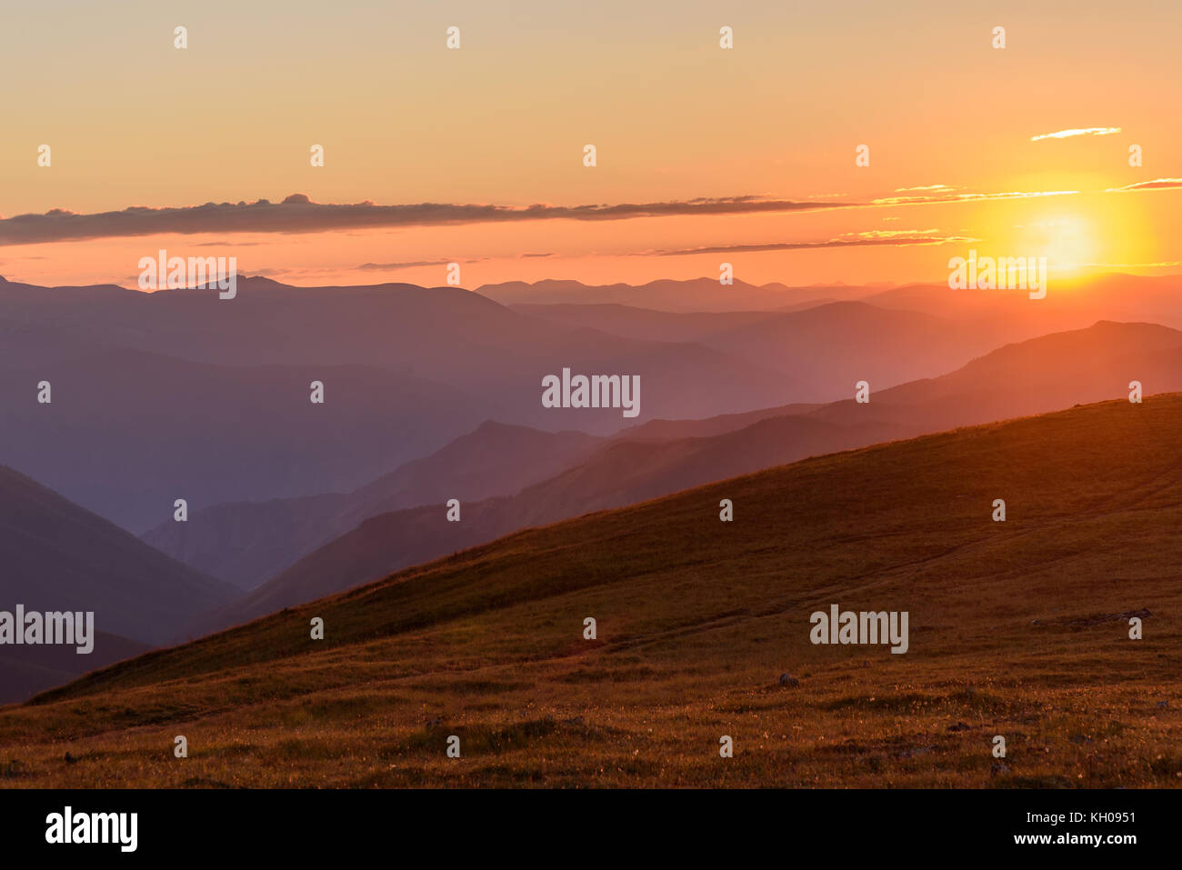 La pittoresca vista delle montagne, il sole e i contorni delle cime di montagna nella luce del sole al tramonto Foto Stock