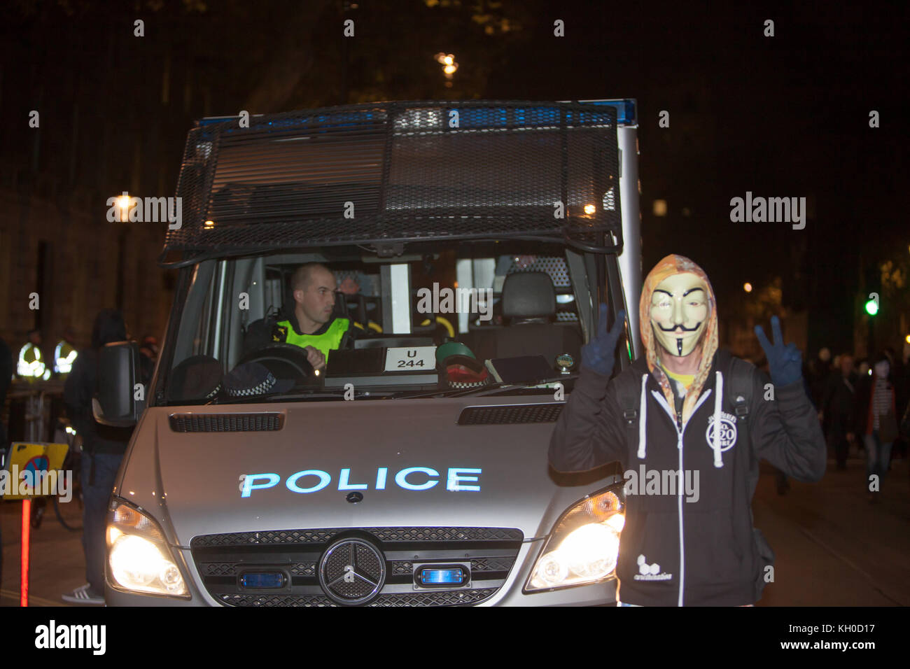 Un protestore con una maschera Guy Fawkes si pone di fronte a una macchina della polizia e mostra il segno di pace con le dita in occasione della Million Mask March annuale a Londra. REGNO UNITO, 05/11 2014. Foto Stock Un protestore con una maschera Guy Fawkes si pone di fronte a una macchina della polizia e mostra il segno di pace con le dita in occasione della Million Mask March annuale a Londra. REGNO UNITO, 05/11 2014. Foto Stock