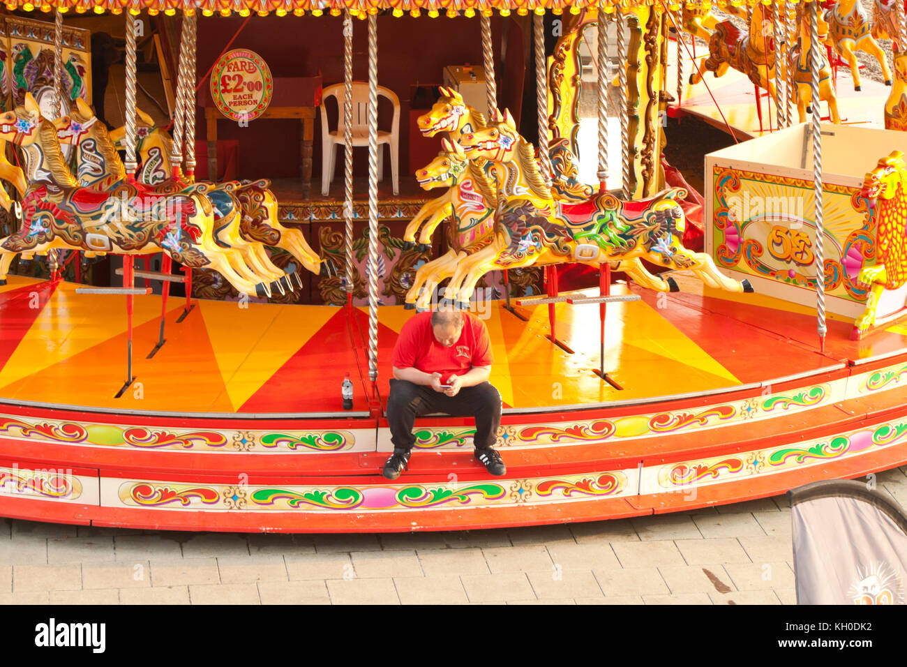 Un lavoratore della fiera guarda al telefono seduto su un merry-go-round sul lungomare di Brighton Foto Stock