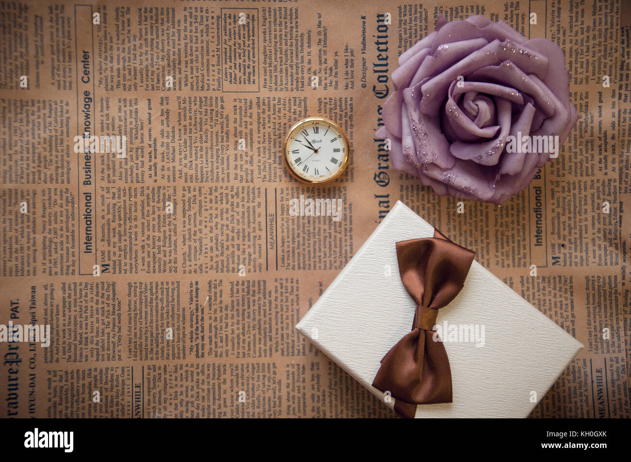 Confezione regalo rosa e orologio da tasca su marrone vecchio giornale Foto Stock