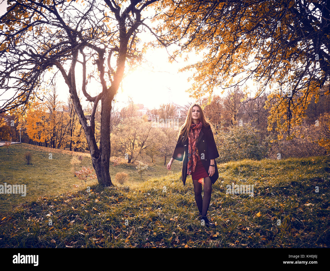 Una ragazza in un mantello nero passeggiate attraverso il giardino in autunno. gialla foglie degli alberi riempite la terra attorno a. Esso è caldo clima soleggiato. Foto Stock