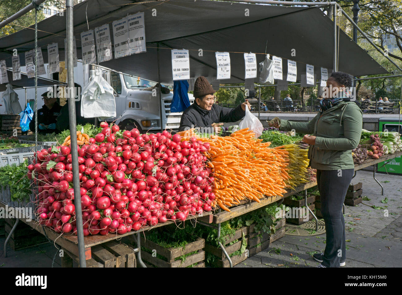 Un americano africano donna acquisti verdura da un americano asiatico uomo presso la Union Square Mercato verde a Manhattan, New York City. Foto Stock