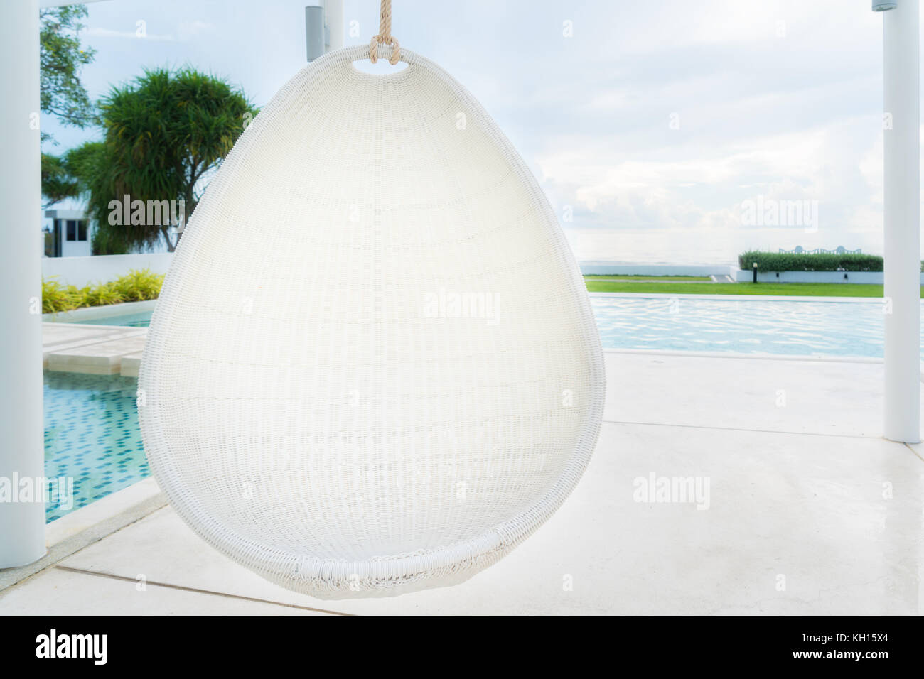Rilassante white rattan sedia pensili a piscina sul mare per vacanza, estate e concetto di viaggio. Foto Stock