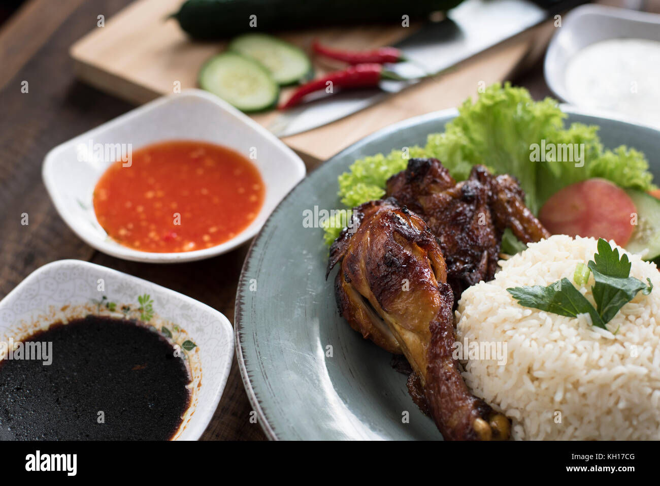 Preparazione del popolare piatto malese nasi ayam o pollo con riso cotto pollo a pezzi, pomodoro, cetriolo, insalata, zuppa, la salsa di soia e salsa di peperoncino. Foto Stock