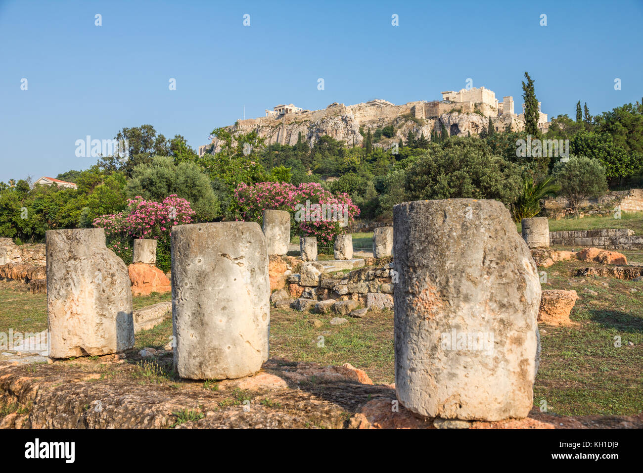 Resti di edifici in Atene antica agora, alberi fioriti e la verticale pendici dell'acropoli in background Foto Stock