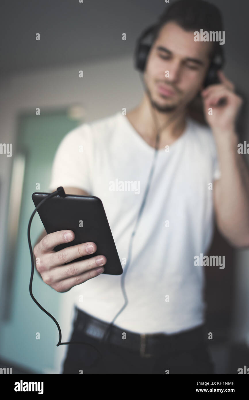 Giovane uomo caucasico ascoltando musica dal tablet a casa, la profondità di campo, tecnologia wireless Foto Stock