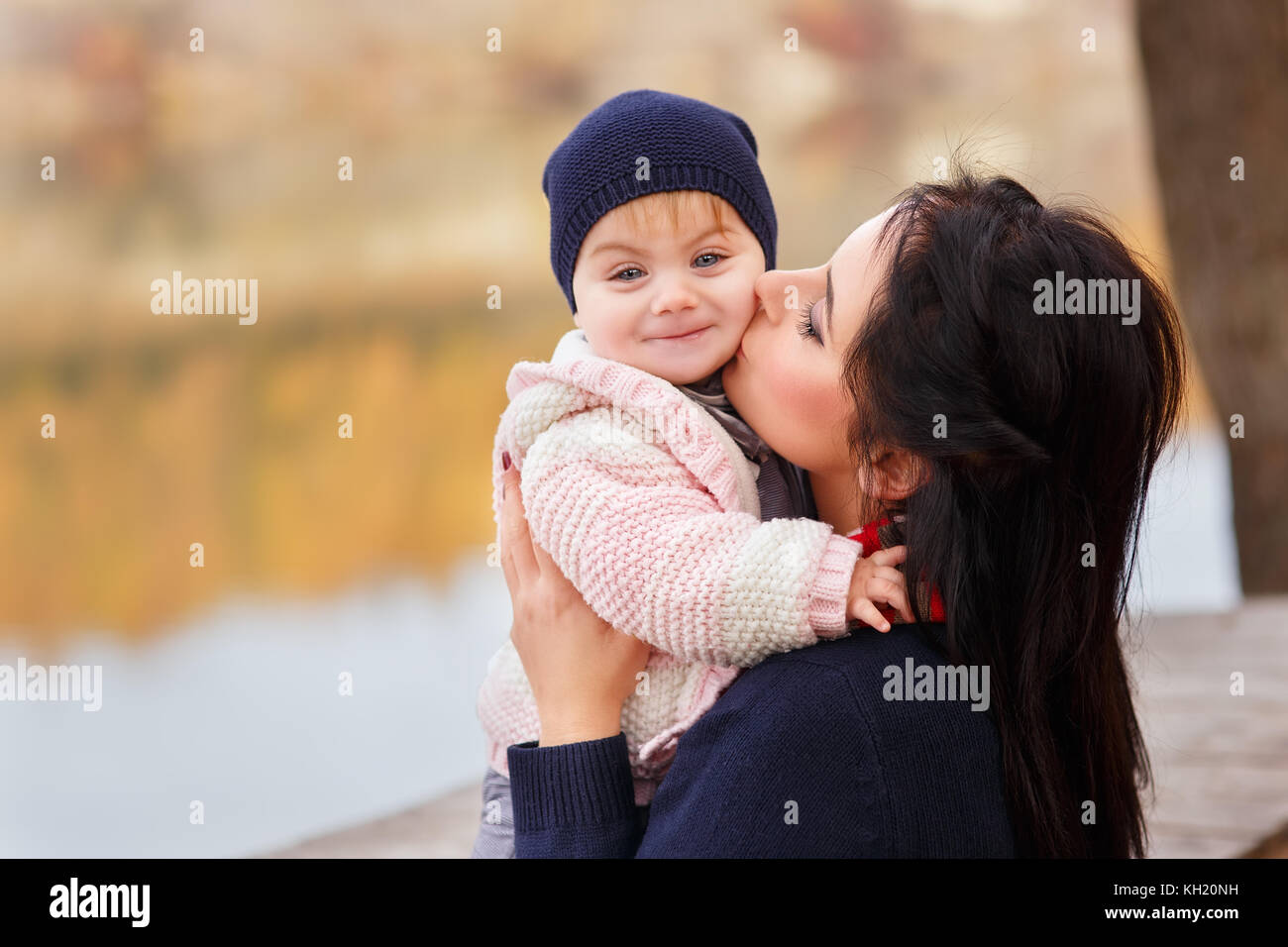 Giovane madre baci piccola figlia in autunno foresta vicino al fiume. mom holding Baby girl in mani. famiglia felice, amore parentale stagione autunnale concep Foto Stock