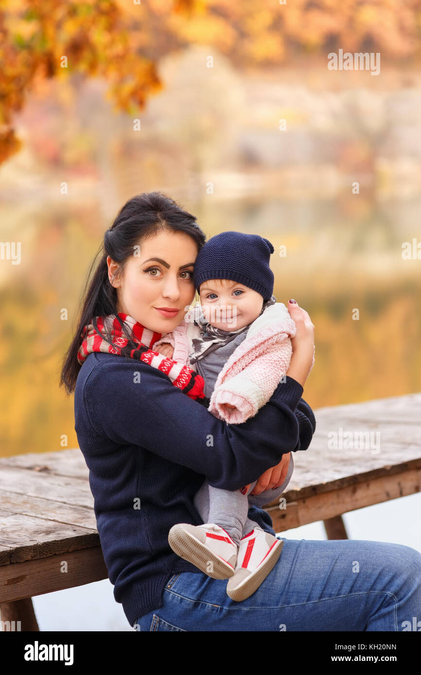 Ritratto di giovane madre con piccola figlia in autunno foresta vicino al fiume. mom holding Baby girl in mani. famiglia felice, amore parentale, mare d'autunno Foto Stock