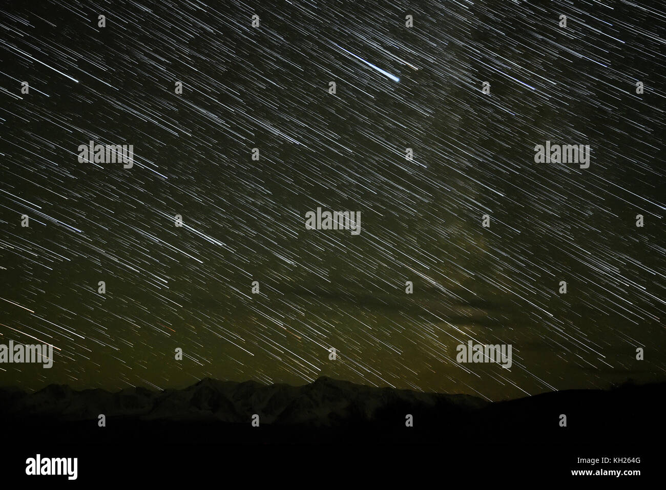 Bella vista notturna del cielo stellato con tracce di stelle cadenti sotto forma di tracce sullo sfondo dei contorni delle montagne innevate e il segnale di PEA Foto Stock