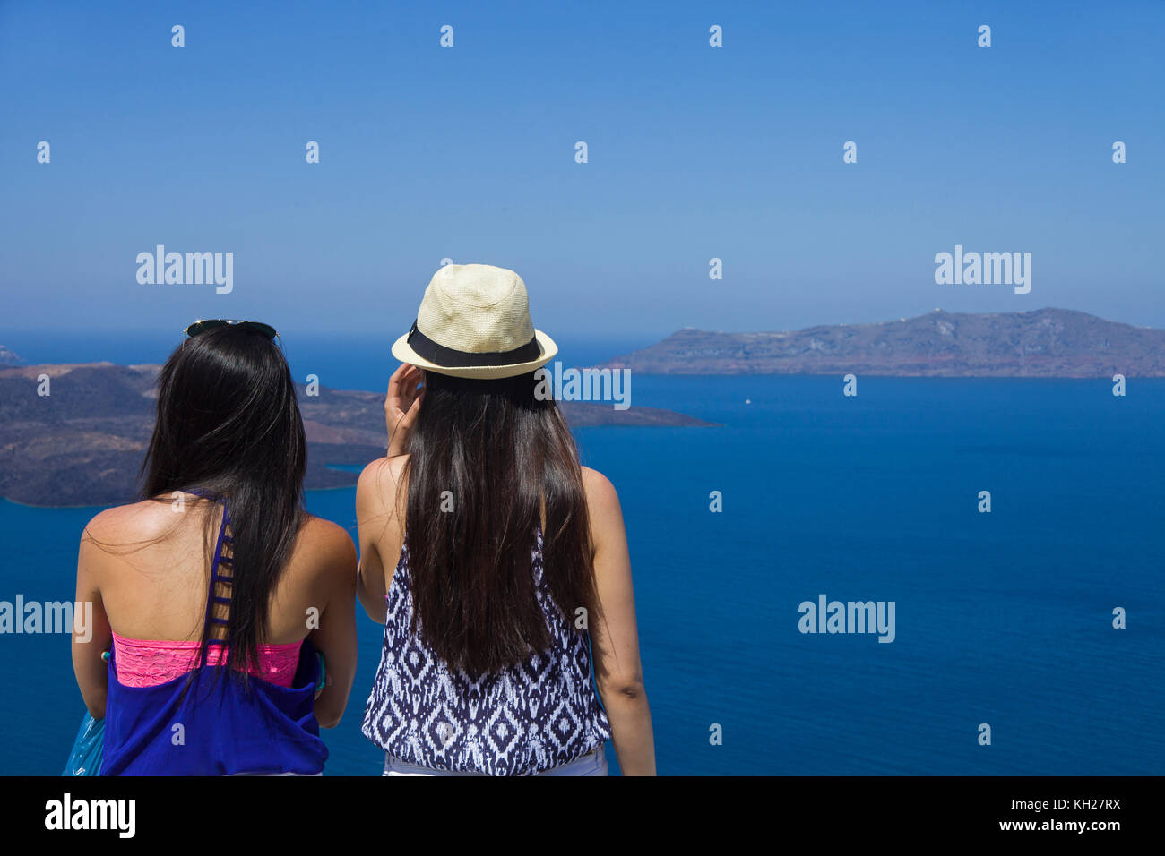 Due ragazze godendo la vista dal bordo del cratere percorso in corrispondenza di Thira di Caldera e Nea Kameni island, SANTORINI, CICLADI Grecia, Mare Mediterraneo, Europa Foto Stock