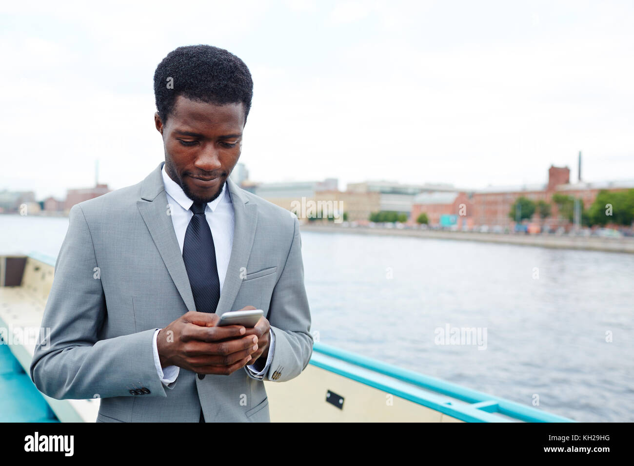 Imprenditore in elegante abito grigio leggendo il messaggio o i messaggi di testo in smartphone all'aperto durante i viaggi Foto Stock