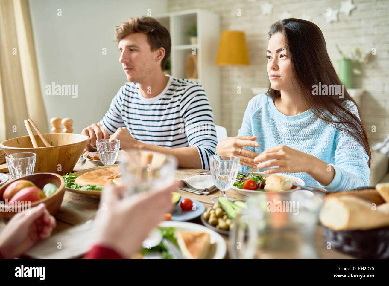 Ritratto di due moderni giovani seduti al grande tavolo con il cibo a cena con gli amici e di ascolto conversazione celebrare la vacanza con f Foto Stock