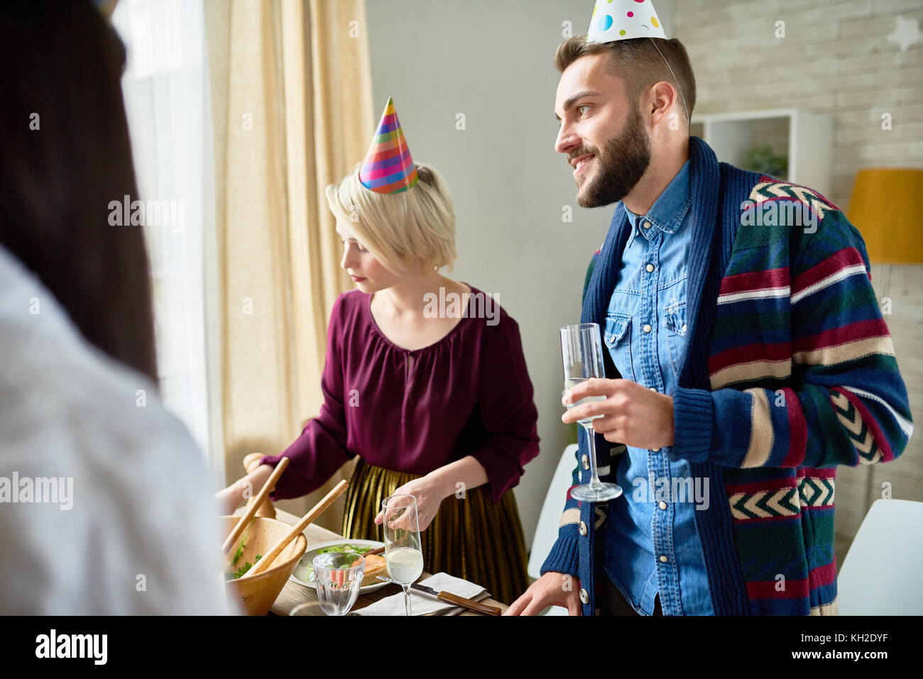 Gruppo di felice giovani indossano cappucci vacanze festeggia il compleanno con gli amici di contenimento bicchieri di champagne durante il party a casa Foto Stock