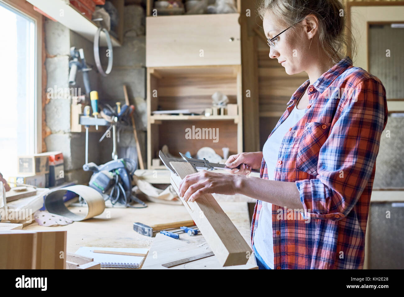 Vista laterale ritratto di donna moderna falegname misura parte in legno mobili al di sopra del tavolo di lavoro in officina Foto Stock