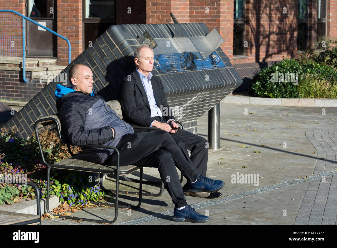 Due uomini godendo il calore del sole invernale sulle rive del fiume Tamigi di fronte alla città di Londra Scuola, Queen Victoria Street, Londra Foto Stock