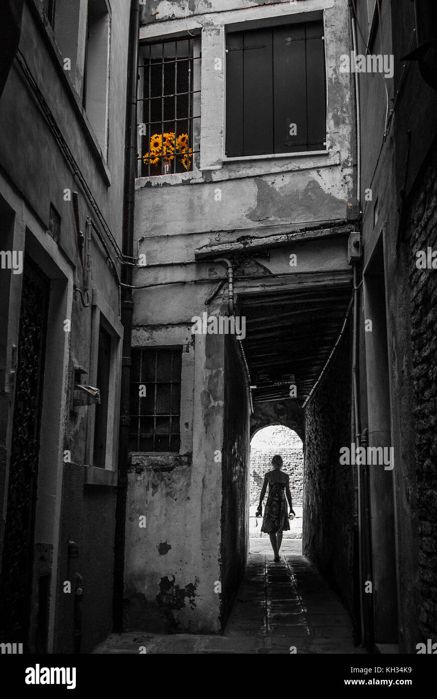 Ragazza camminare anche se un vicolo in Venezia con alcuni campi di girasoli in una finestra al piano di sopra. Raffigurante il viaggio e alla scoperta di Venezia come da soli traveler. Foto Stock