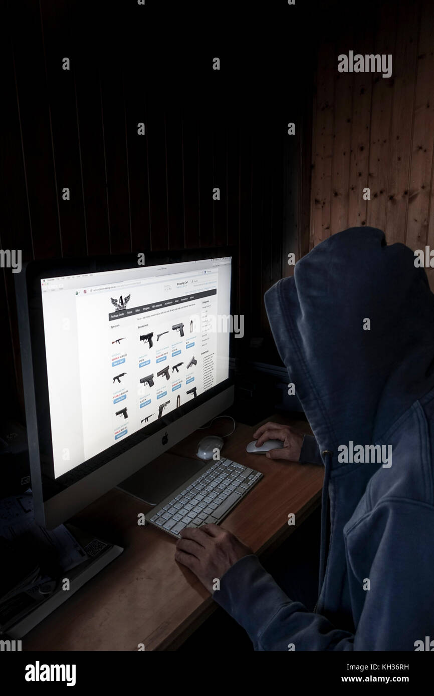 Concetto di immagine di incappucciati cyber criminali, uomo utilizzando il computer per accedere a internet profondo pagina web offrendo pistole, Foto Stock