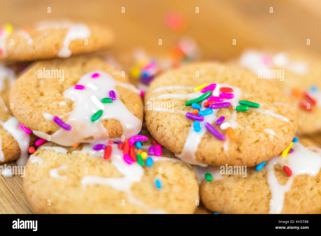 Appena sfornati i cookie di zucchero con glassa bianca e colorata arcobaleno spruzza sulla tavola di legno, fuoco selettivo Foto Stock