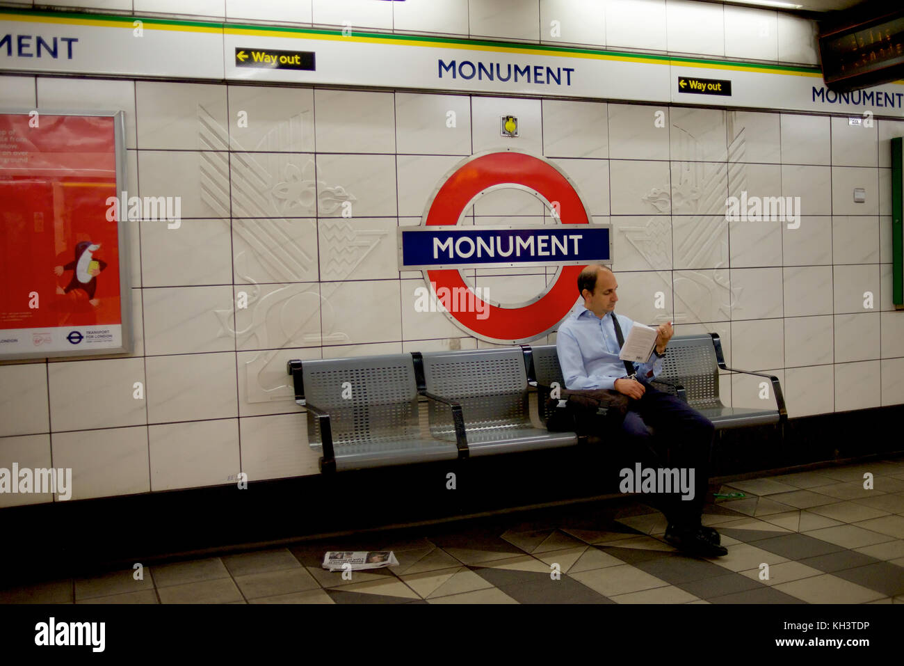 Uomo di lettura su un banco a monument station sulla metropolitana di londra Foto Stock