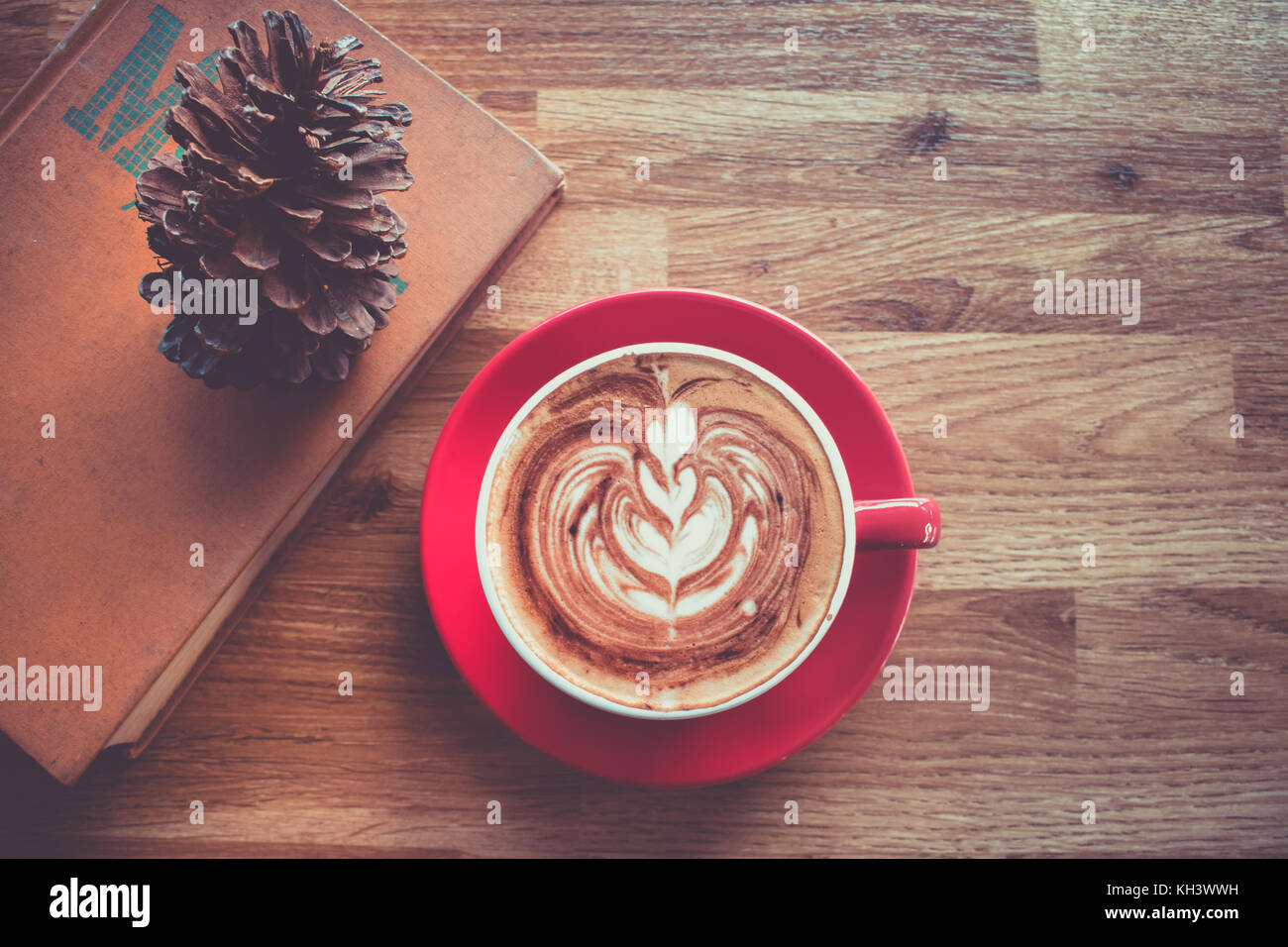 Caffè latte art in red cup con un libro di testo sulla tavola di legno Foto Stock