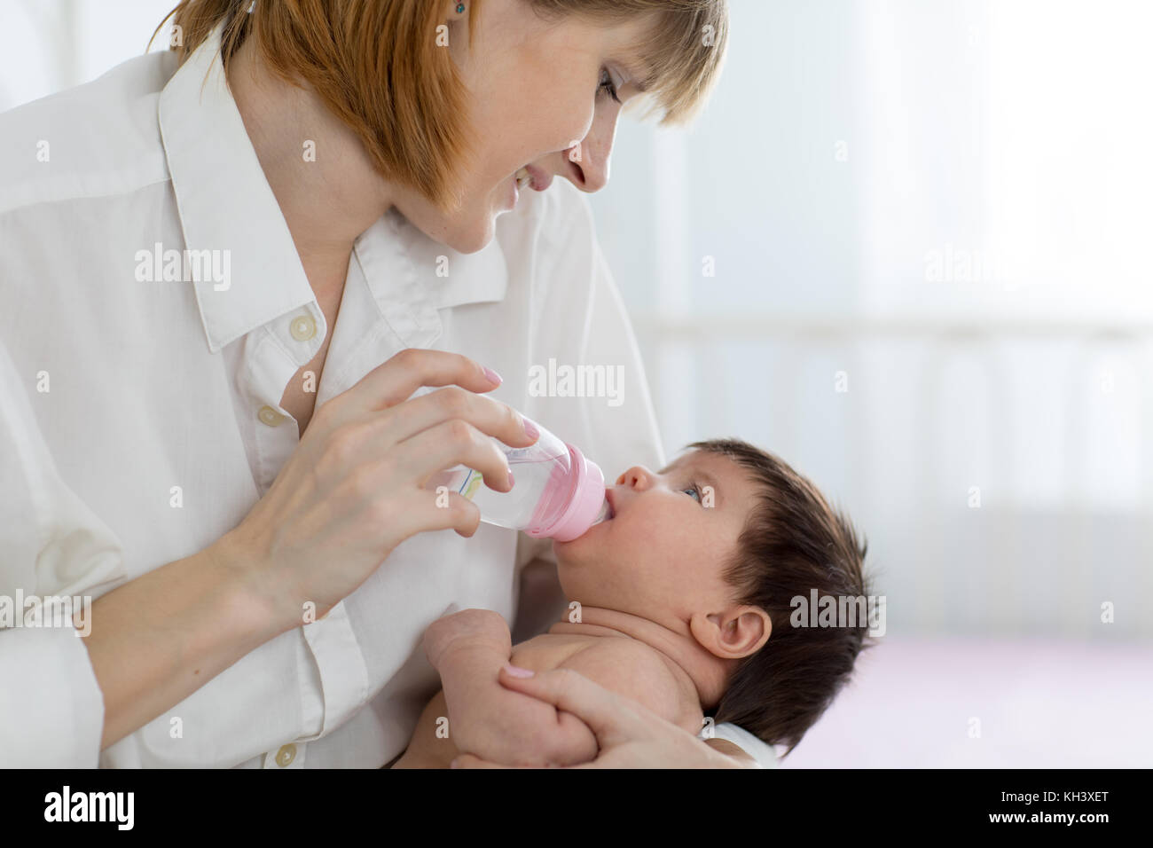 Mom dando baby acqua dalla bottiglia seduta sul letto Foto Stock