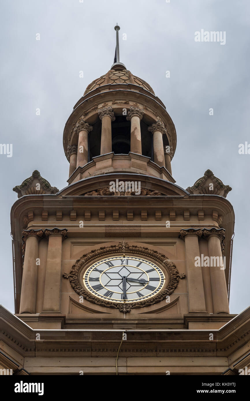 Sydney, Australia - 25 marzo 2017: primo piano della parte superiore di colore marrone stone town hall clock tower. bianco e oro tempo pezzo pesante contro il cielo grigio. Foto Stock