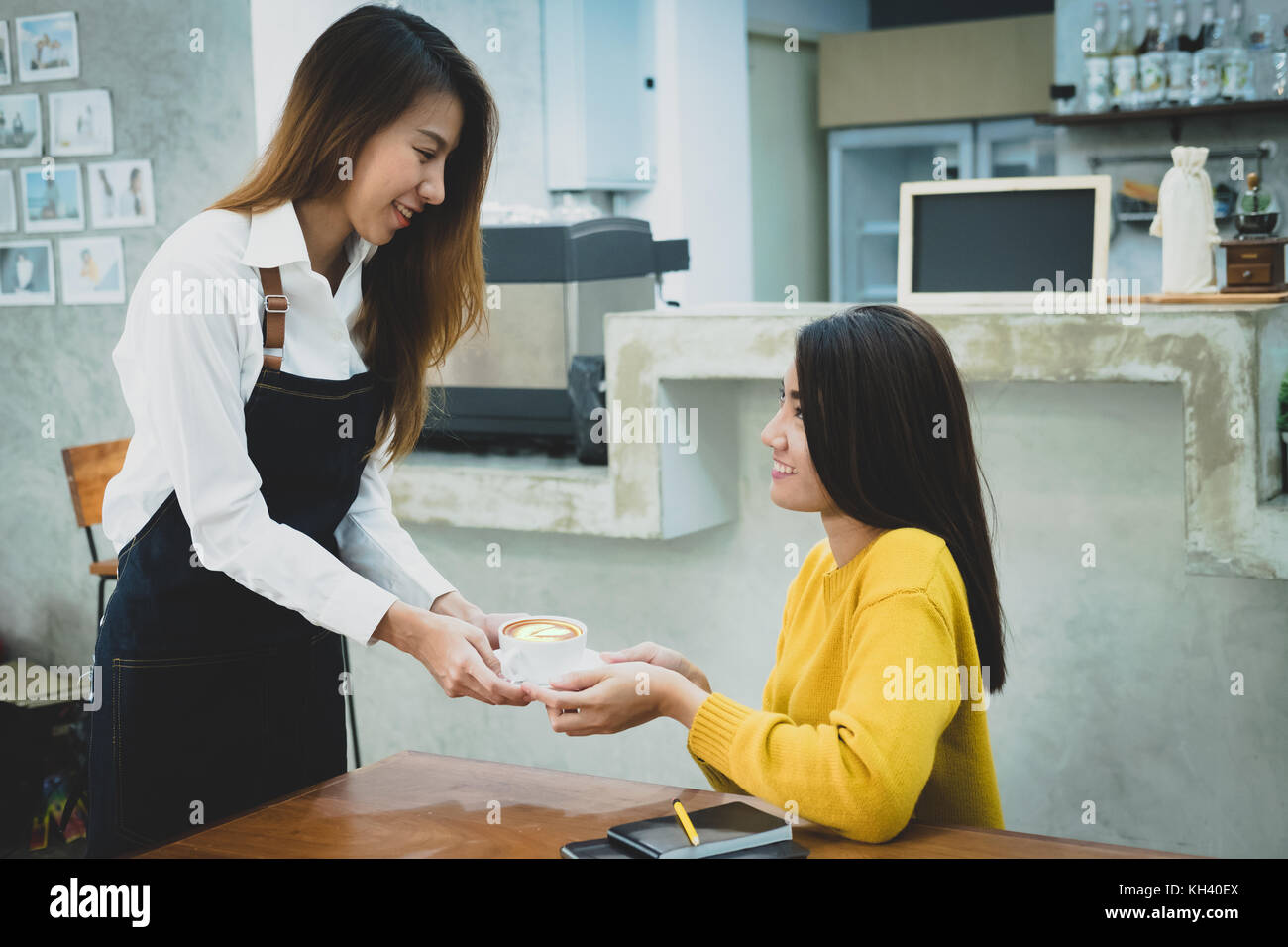 Sorridente asian barista serve una tazza di caffè al cliente. Il cafe ristorante servizio, industria alimentare e delle bevande del concetto. Foto Stock