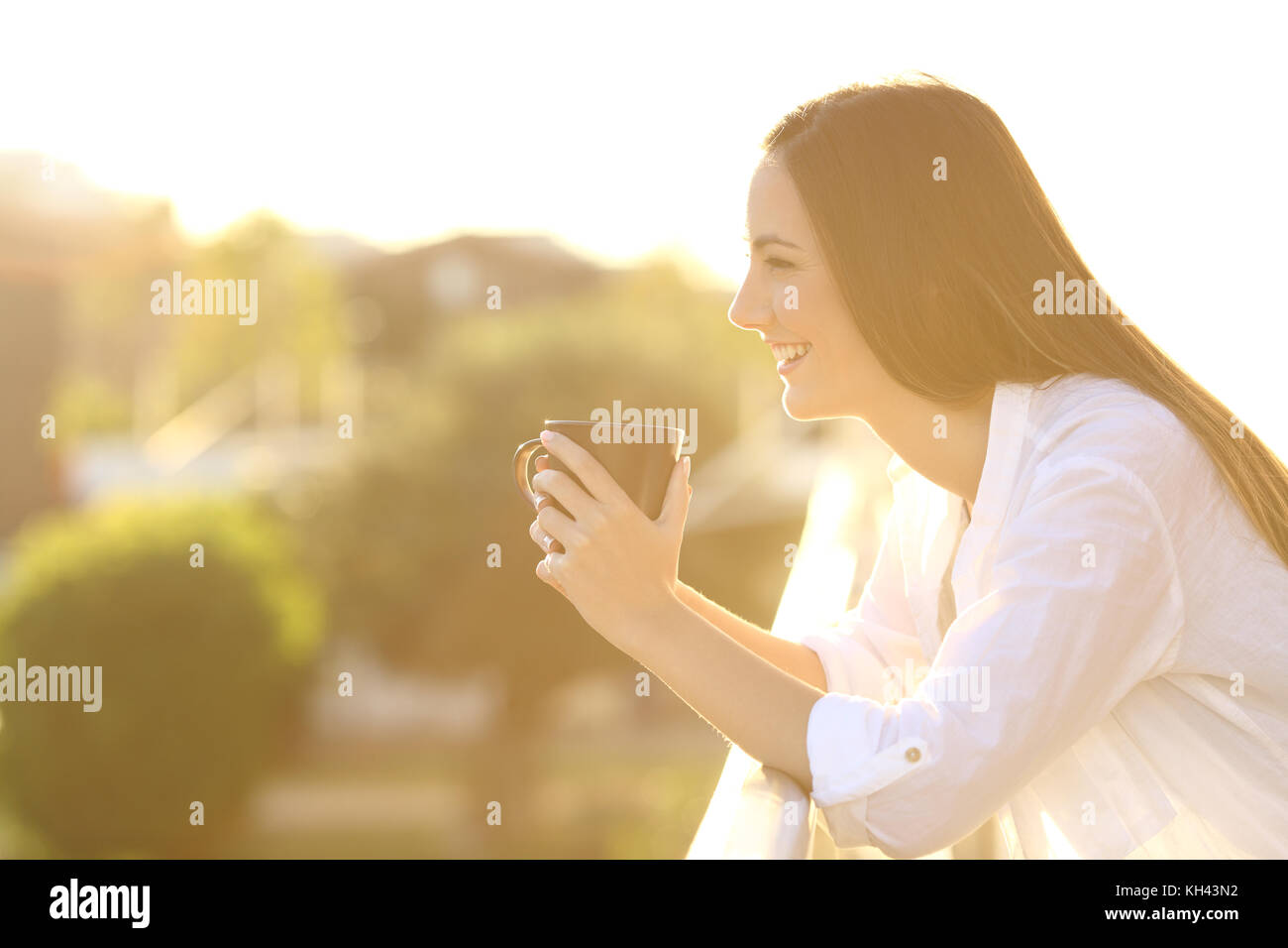 Vista laterale di un felice proprietario di casa rilassarsi bevendo un caffè in una terrazza al tramonto Foto Stock