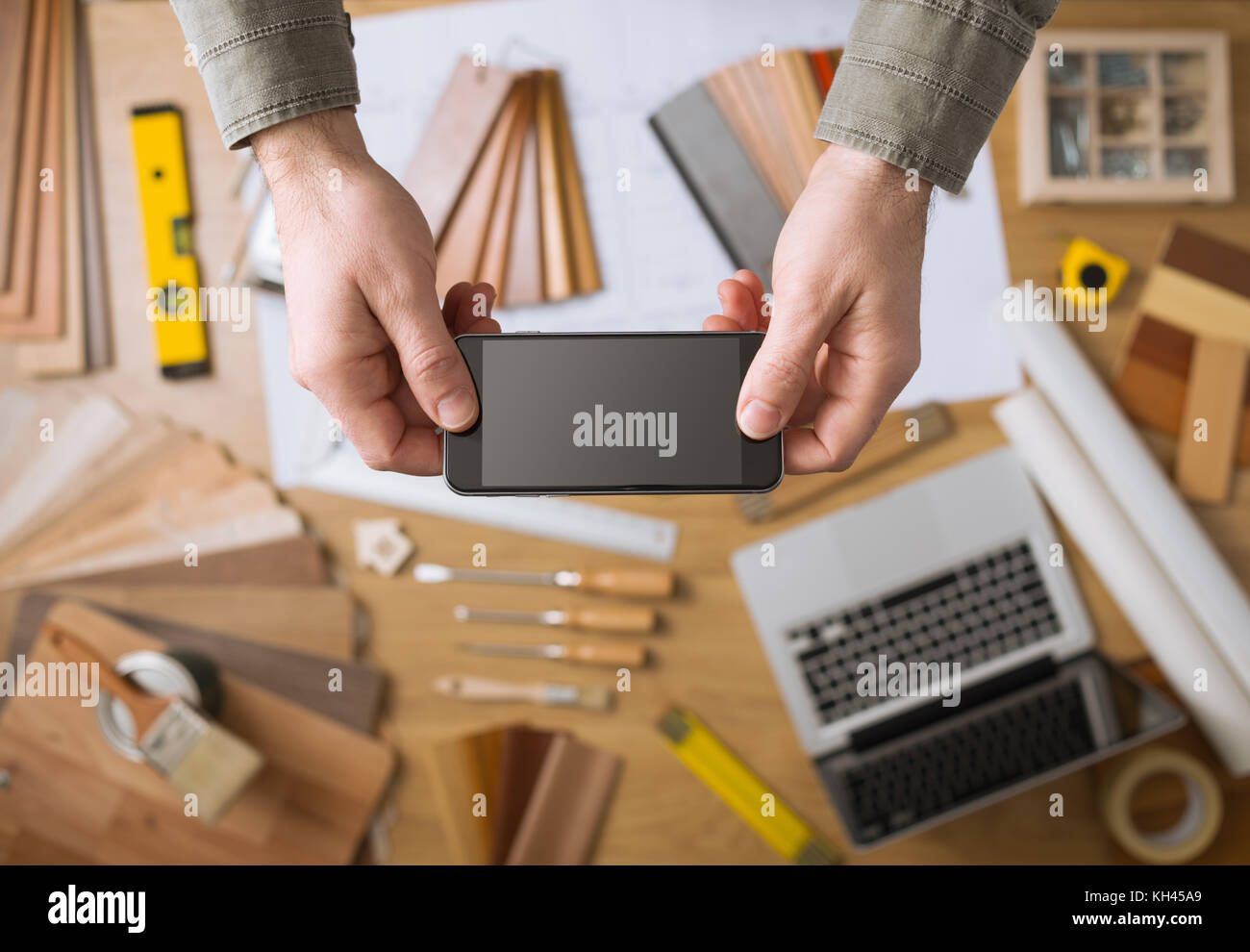 Home decorator le mani tenendo un touch screen mobile phone, desktop con strumenti, laptop e campioni di legno su sfondo, vista dall'alto Foto Stock