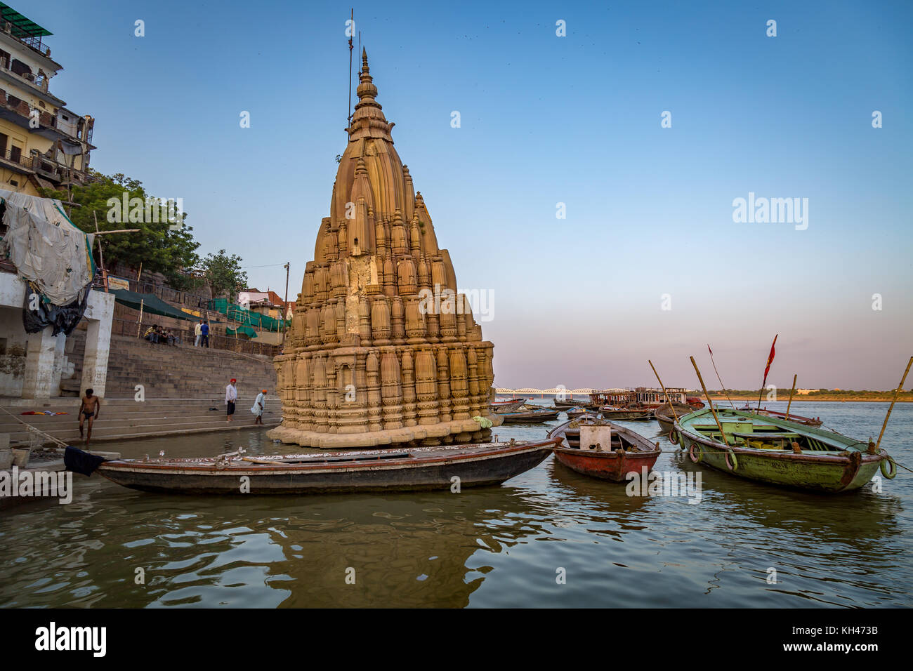 Varanasi gange fiume ghat con vista di un antico tempio sommerso in acqua e barche di legno ancorato vicino alla riva del fiume. Foto Stock