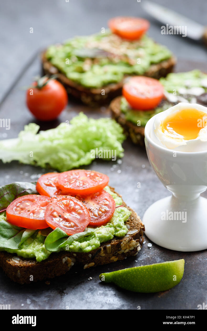 Avocado toast con spinaci, pomodoro e uova sode. Verde sano veggie sandwich aperto. Messa a fuoco selettiva Foto Stock