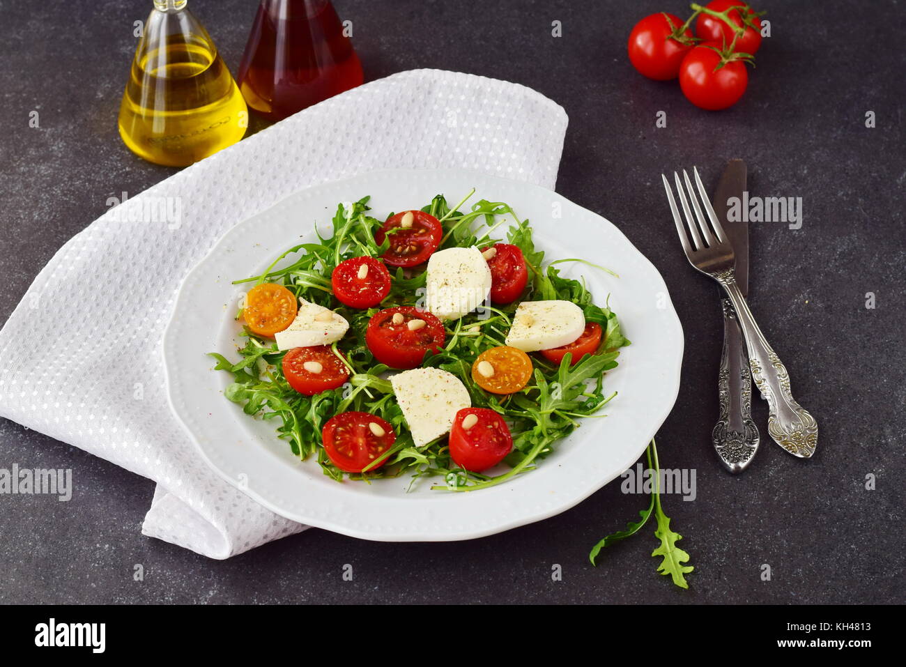 Tradizionale italiano con insalata di pomodoro ciliegino, rucola, mozzarella, olio di oliva aceto di vino su una piastra bianca su un grigio Sfondo astratto. Foto Stock