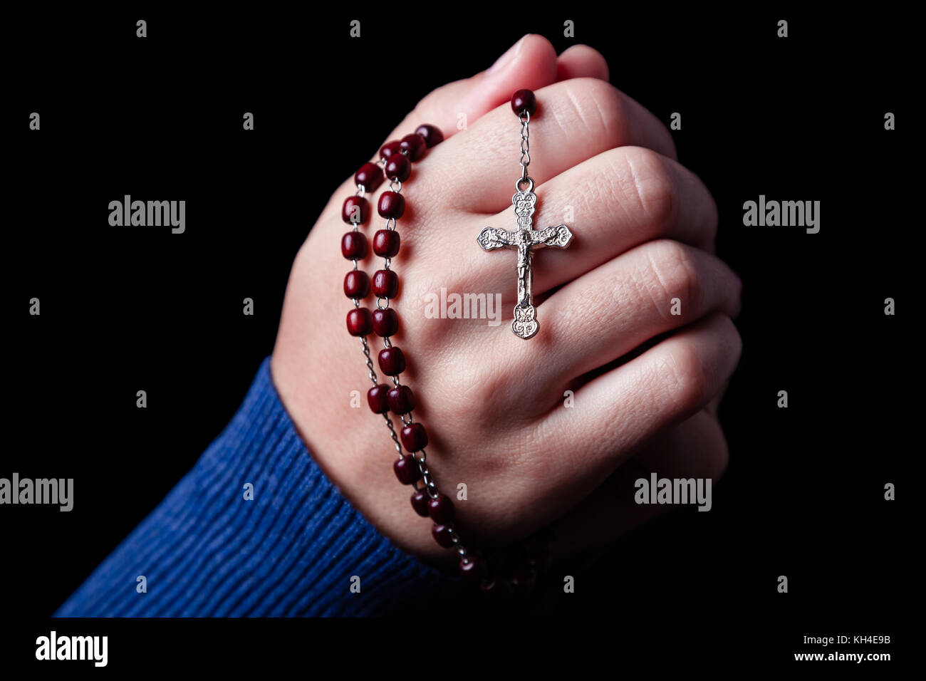 Mani femminili pregando tenendo un rosario con Gesù Cristo in croce o crocifisso su sfondo nero. donna con cristiana fede cattolica mano Foto Stock