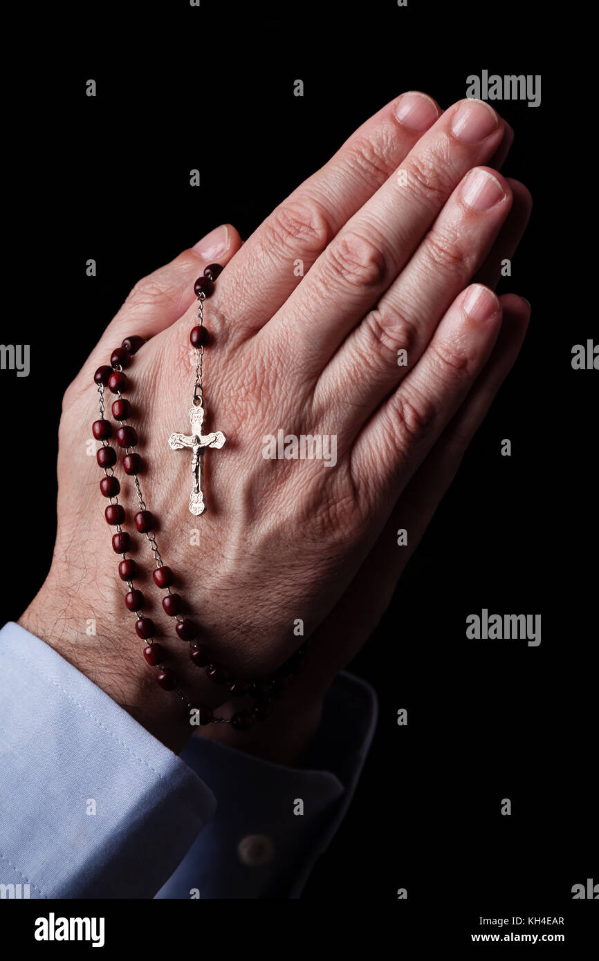Mani maschio pregando tenendo un rosario con Gesù Cristo in croce o crocifisso su sfondo nero. uomo maturo con cristiana cattolica fede religiosa Foto Stock