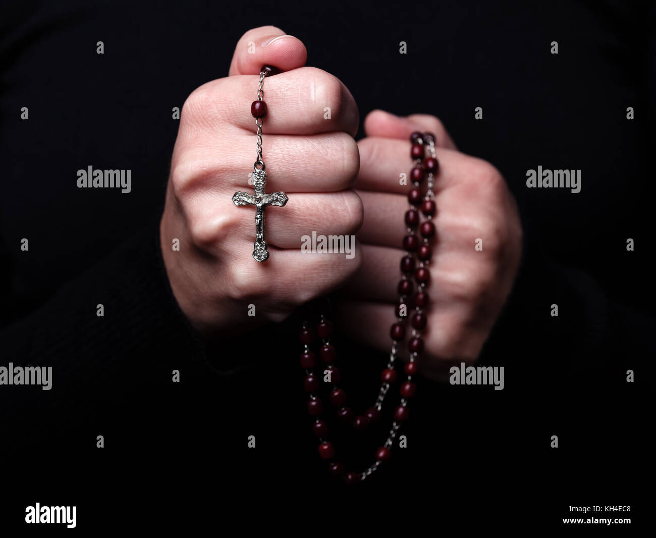 Mani femminili pregando tenendo un rosario con Gesù Cristo in croce o crocifisso su sfondo nero. donna con cristiana cattolica fede a mano Foto Stock