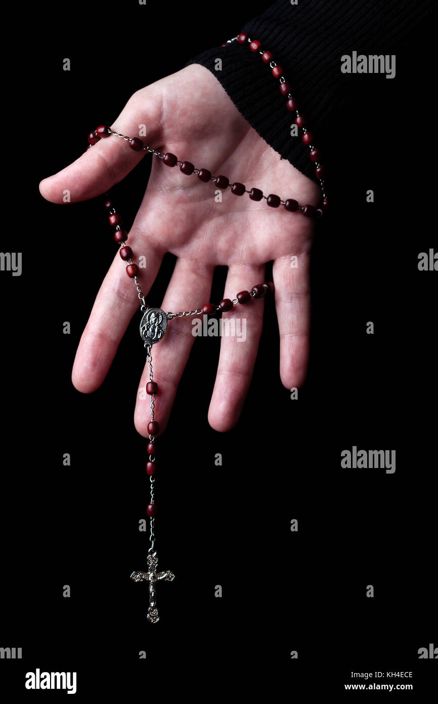 Mani femminili holding e appendere un rosario con Gesù Cristo in croce o crocifisso su sfondo nero. donna con cristiana cattolica fede religiosa Foto Stock